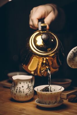 person-holding-gold-teapot-pouring-white-ceramic-teacup-230490