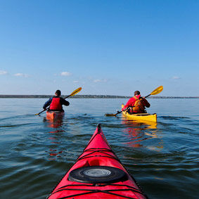 Two guys in a kayak. Kayaking in the calm blue lake. View from the red kayak.